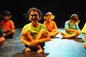 crianças sentadas com óculos gigante no rosto em uma apresentaçao de dança