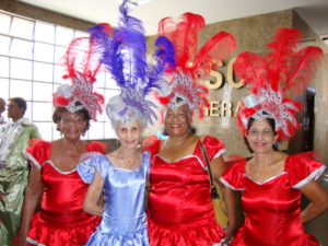 mulheres com vestidos e adereço de cabeça com plumas cores vermelho e lilás