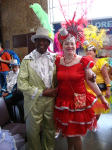 casal homem negro de fraque vesde claro e mulher branca de vestido vermelho com adereço de cabeça