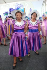 duas mulheres vestidas com vestidos cor lilás e azul com chapéu