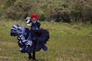 pessoa dançando com figurino azul e máscara barnca e cabelo vermelho