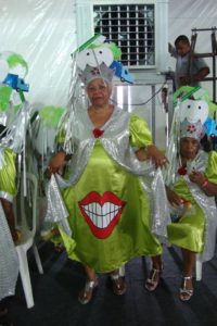 mulher vestida com fantasia de carnaval verde prateado e vermelho com adereço de cabeça e sorriso no vestido