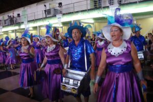 várias mulheres vestidas com fantasia vestido lilás e chapéu branco e dois vestidos de fantasias azul com chapéu