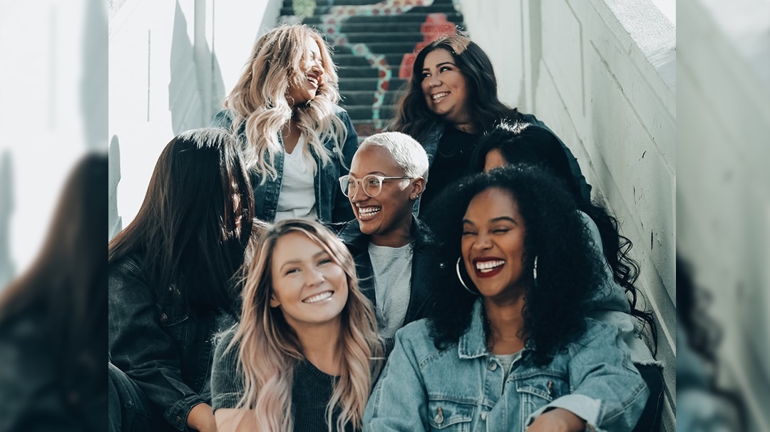 sete mulheres sentadas na escada sorrindo olhando uma para outra