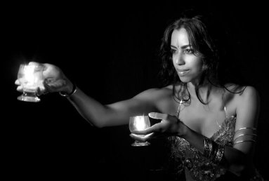 foto preto e branco mulher morena cabelos pretos com duas taças com fogo nas maos dançando dança do ventre